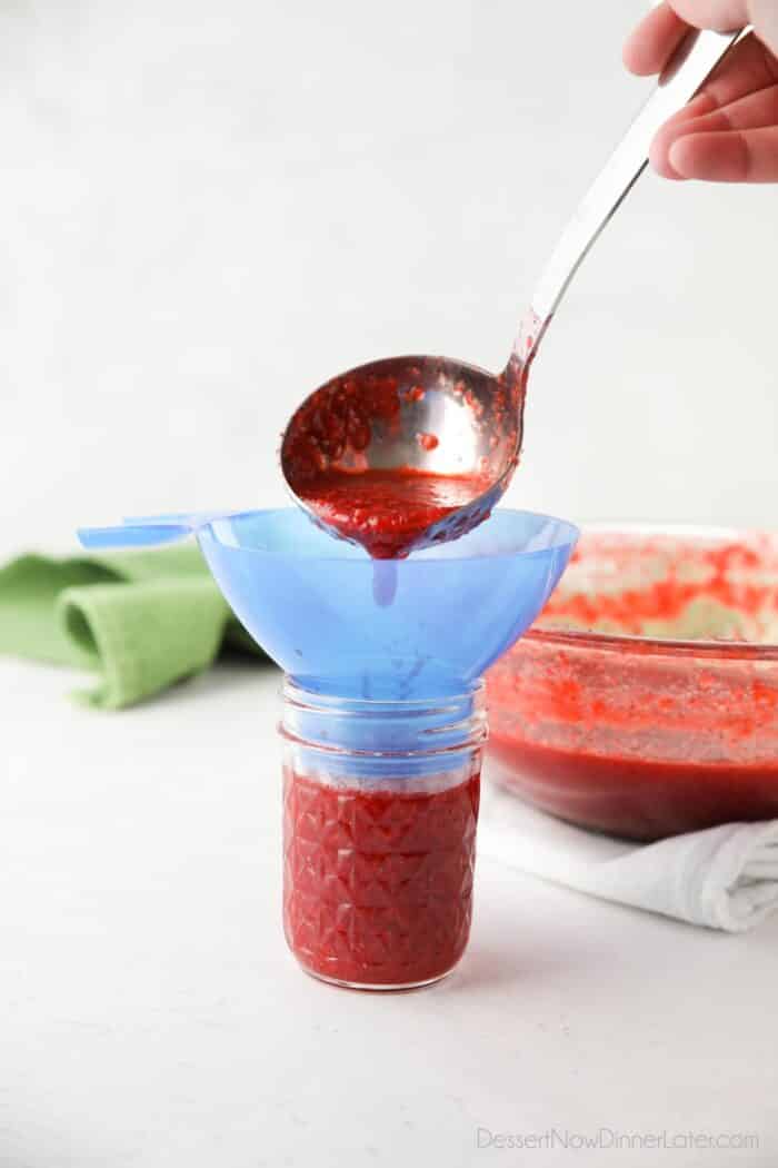 Pouring strawberry mixture into glass jars for freezer jam.