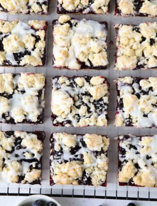 Squares of blueberry pie bars with glaze on top resting on a cooling rack.