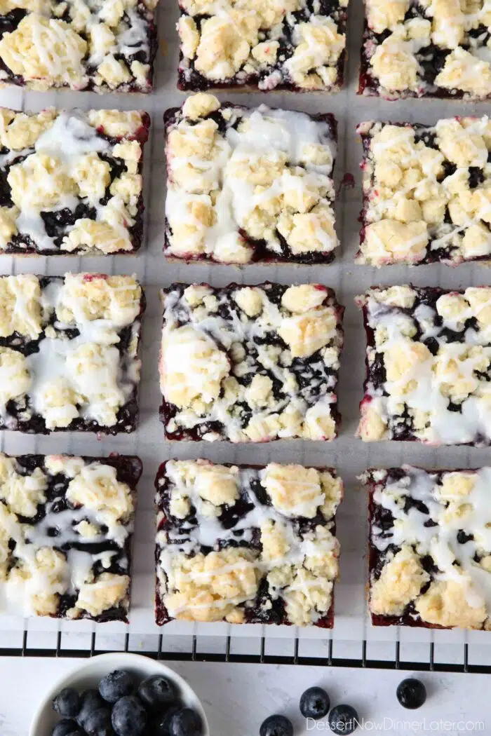Squares of blueberry pie bars with glaze on top resting on a cooling rack.