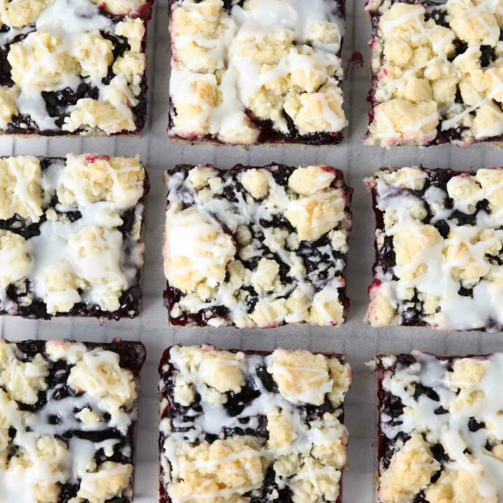 Squares of blueberry pie bars with glaze on top resting on a cooling rack.