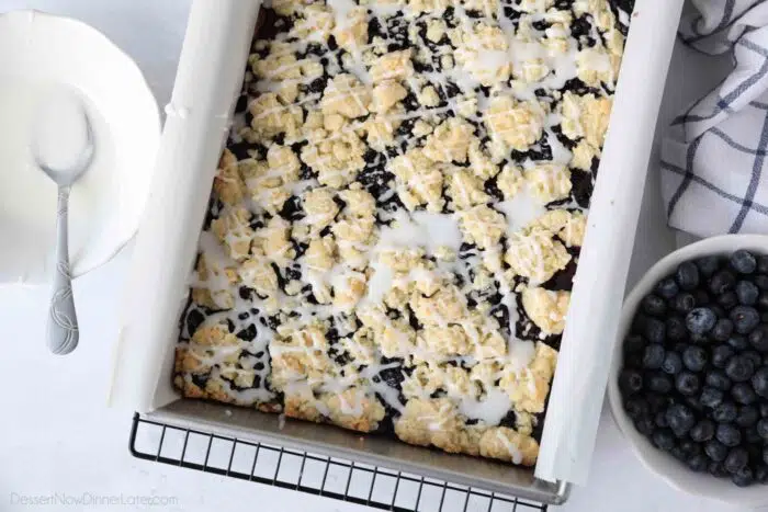 Baked blueberry pie bars in a pan with glaze drizzled on top.