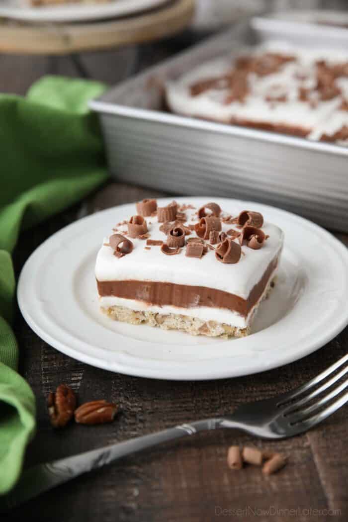 Layered dessert with a pecan crust topped with layers of cream cheese, chocolate pudding, and Cool Whip topped with chocolate curls for decoration.