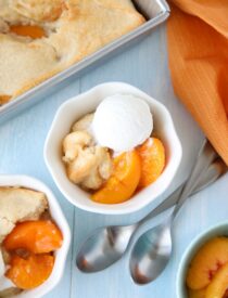 Peach Cobbler with cake batter crust on top and a scoop of vanilla ice cream.