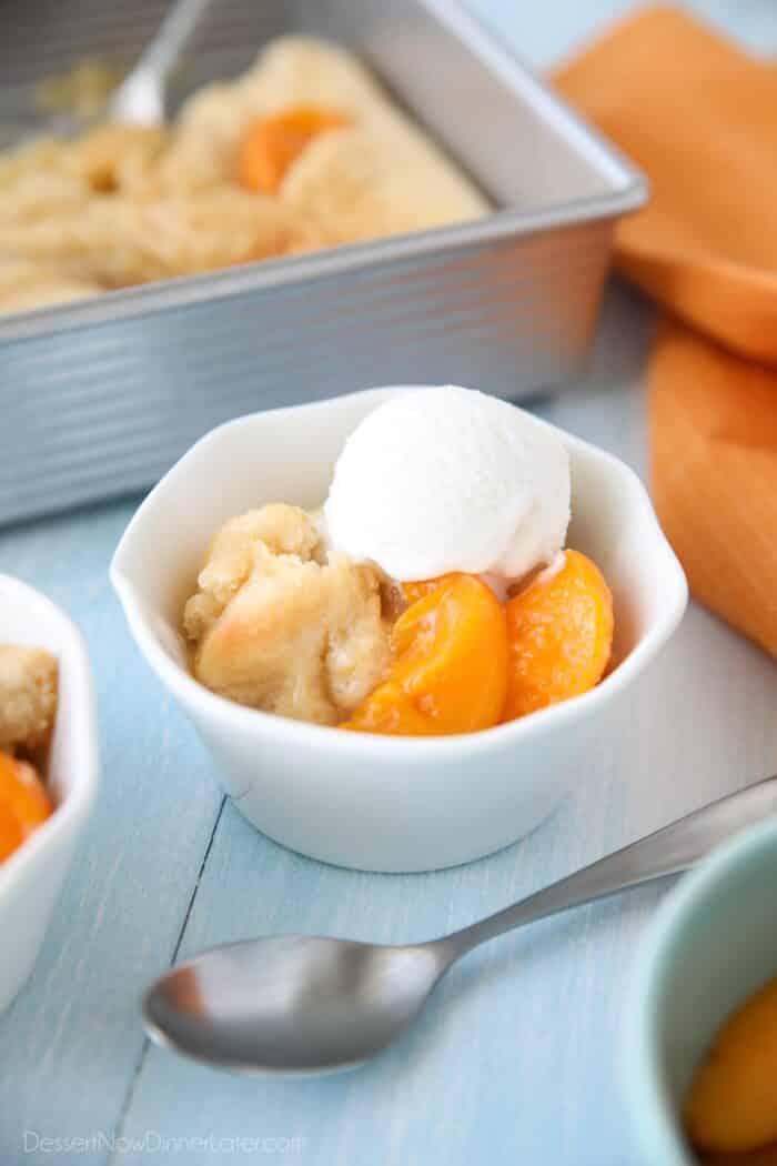 Peach Cobbler with cake batter crust on top and a scoop of vanilla ice cream.