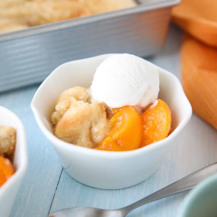 Peach Cobbler with cake batter crust on top and a scoop of vanilla ice cream.