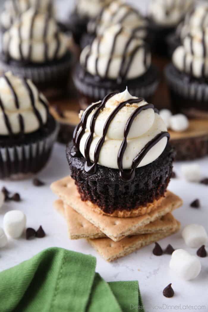 S'mores Cupcakes made with a graham cracker crust, chocolate cake, and marshmallow buttercream frosting topped with chocolate sauce and crushed graham crackers.