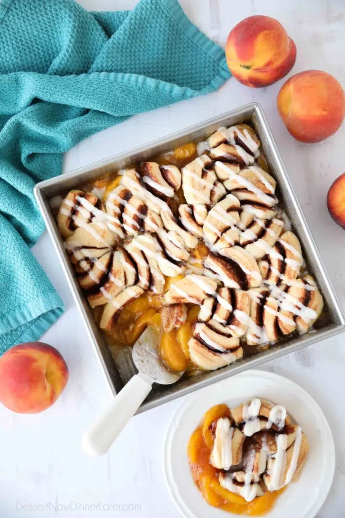 Top view of fresh peach cobbler topped with cinnamon rolls and cream cheese frosting.