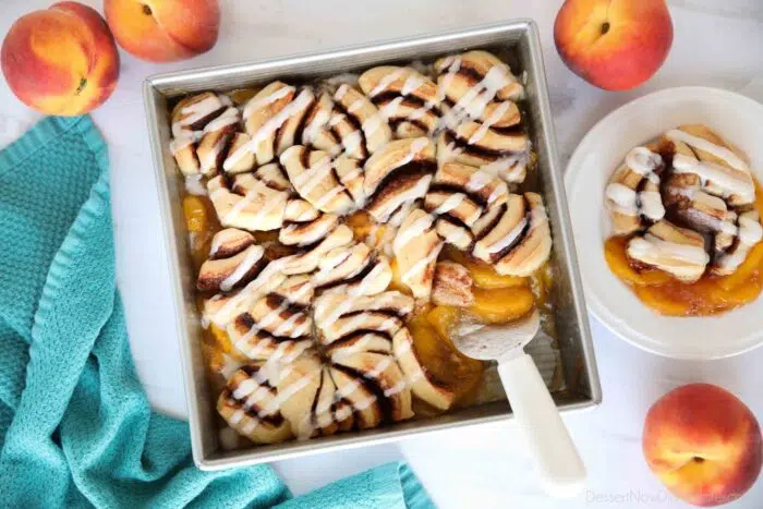 Top view of fresh peach cobbler topped with cinnamon rolls and cream cheese frosting.