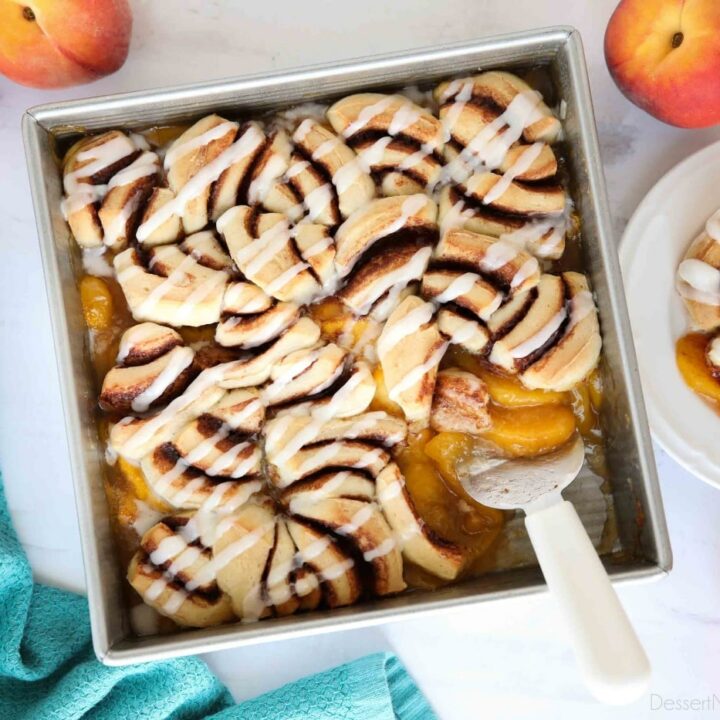 Top view of fresh peach cobbler topped with cinnamon rolls and cream cheese frosting.