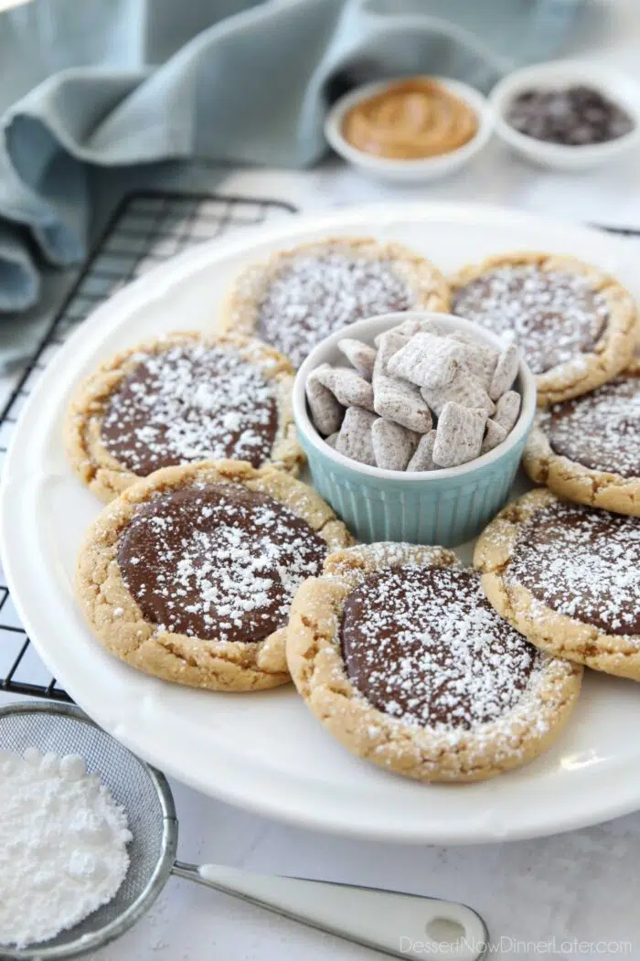 Angled view of a plate of peanut butter chocolate cookies with a bowl of muddy buddies Chex mix in the middle.