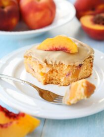 Fork full of peach cake with brown sugar frosting taken out of a slice on a plate.