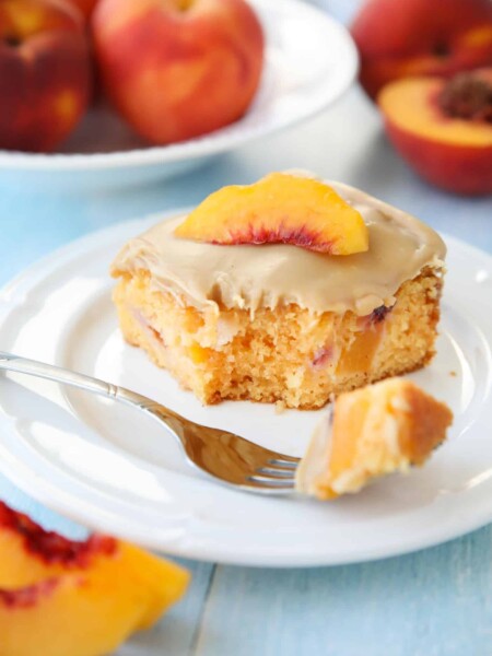 Fork full of peach cake with brown sugar frosting taken out of a slice on a plate.