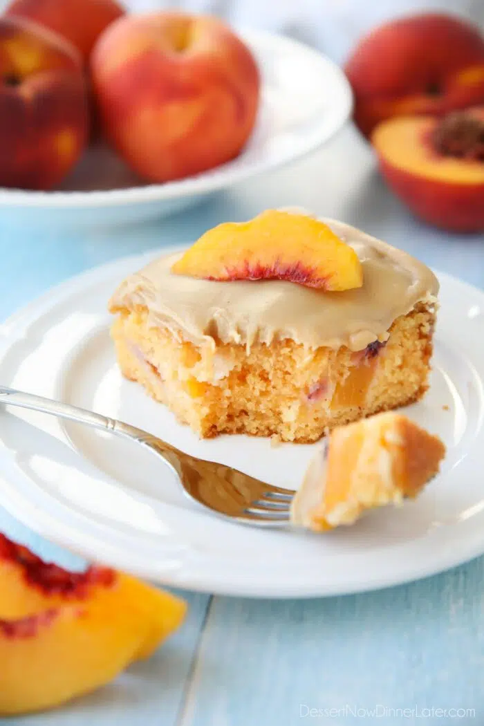 Fork full of peach cake with brown sugar frosting taken out of a slice on a plate.