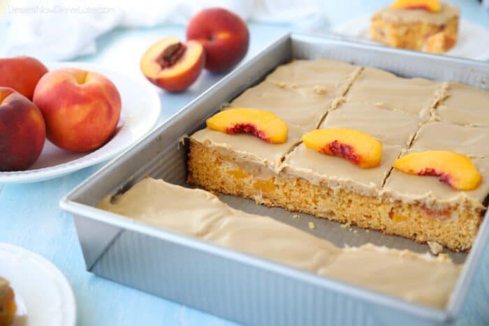 A baked and frosted peach cake inside of a baking pan with sliced peaches on top.