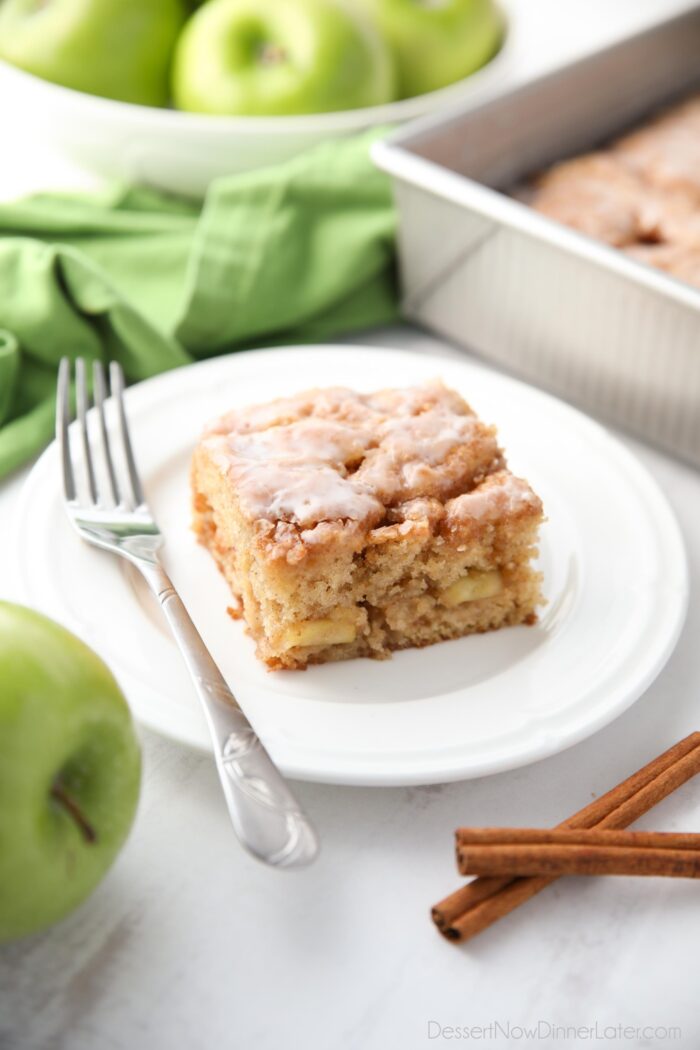 Kvadrātveida glazētas ābolu kūkas gabals uz šķīvja.