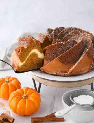 Slice of pumpkin bundt cake with cream cheese filling being served with a spatula.