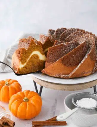 Slice of pumpkin bundt cake with cream cheese filling being served with a spatula.