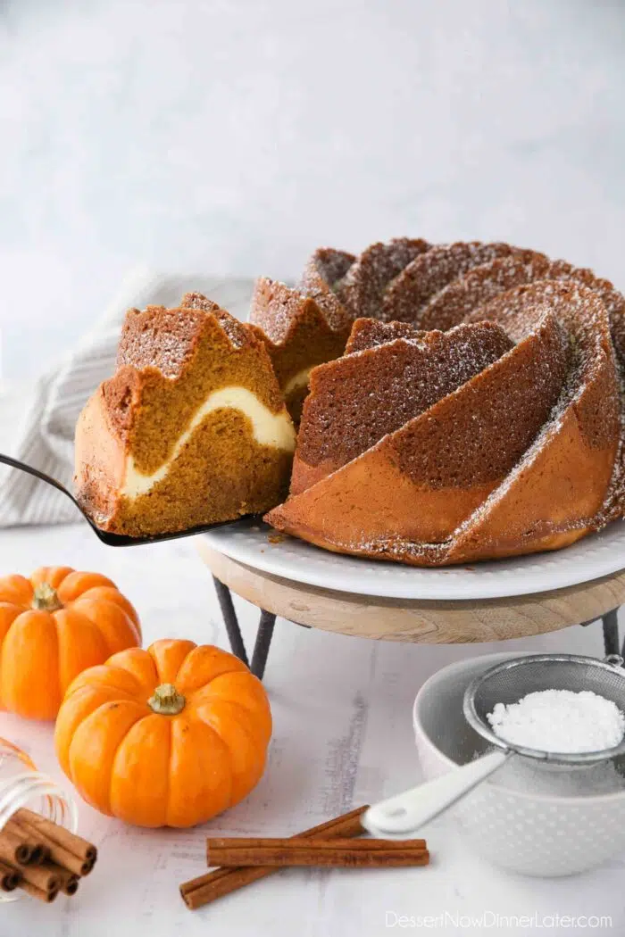 Slice of pumpkin bundt cake with cream cheese filling being served with a spatula.