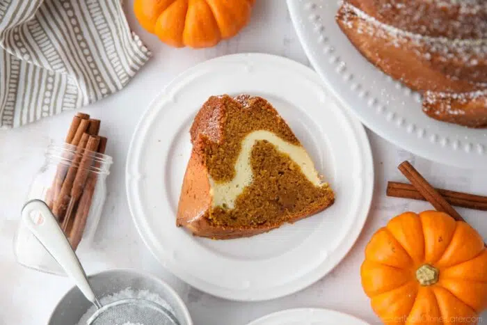 Slice of pumpkin cake with cream cheese swirl on a plate.