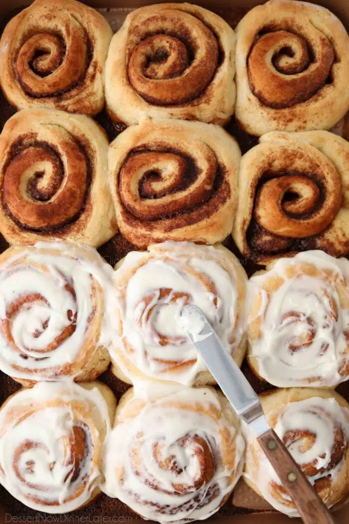 Spreading cream cheese frosting on top of homemade cinnamon rolls.