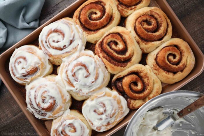 Cinnamon rolls in a pan, half with frosting, and half without.