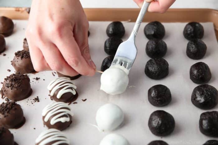 Using a toothpick to place a chocolate dipped Oreo Ball onto parchment paper.