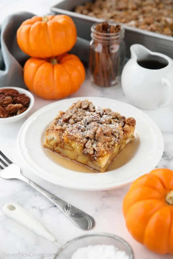 Square piece of pumpkin French toast casserole on a plate with syrup and powdered sugar.