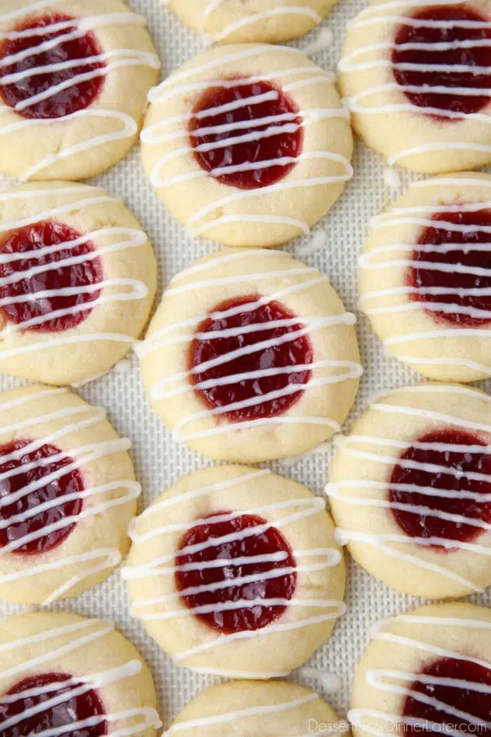 Icing drizzled on top of raspberry thumbprint cookies on a silicone baking mat.