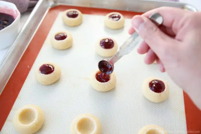 Spooning seedless raspberry jam into cookie wells.