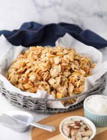 Sweet Chex Mix with coconut and almonds in a large basket lined with parchment paper.