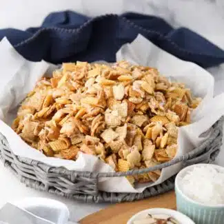 Sweet Chex Mix with coconut and almonds in a large basket lined with parchment paper.