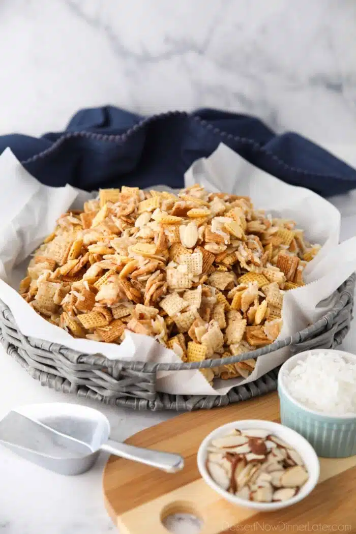Sweet Chex Mix with coconut and almonds in a large basket lined with parchment paper.