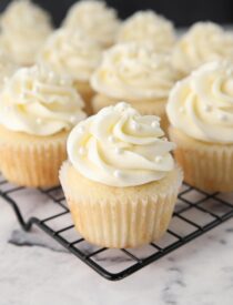 White Cupcakes with vanilla frosting and white sugar pearls on top.