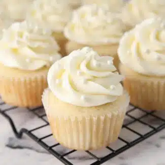 White Cupcakes with vanilla frosting and white sugar pearls on top.