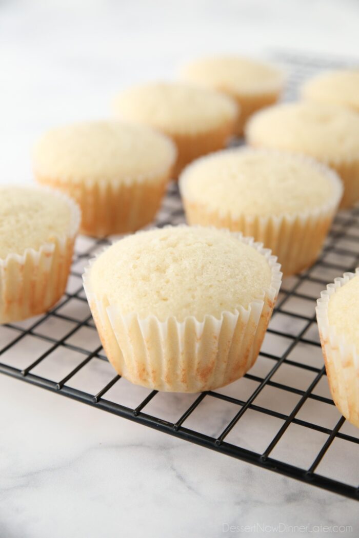 Baked white cupcakes cooling on wire rack.