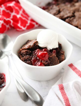 Chocolate cherry dump cake in a small bowl topped with vanilla ice cream.