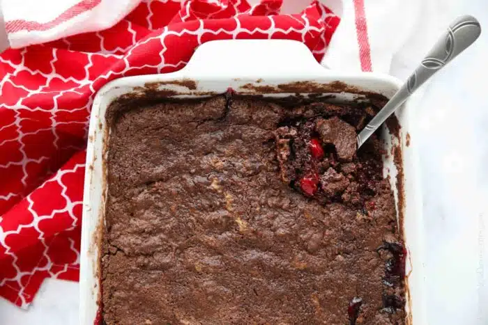 Baked chocolate cherry cobbler in baking dish with a serving spoon.