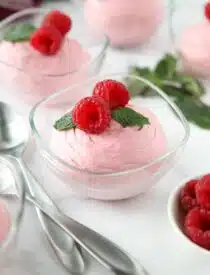 Raspberry Mousse in a small clear bowl with fresh raspberries and mint on top.