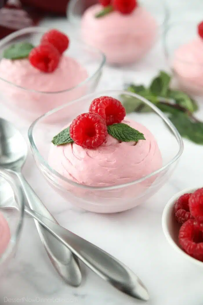 Raspberry Mousse in a small clear bowl with fresh raspberries and mint on top.