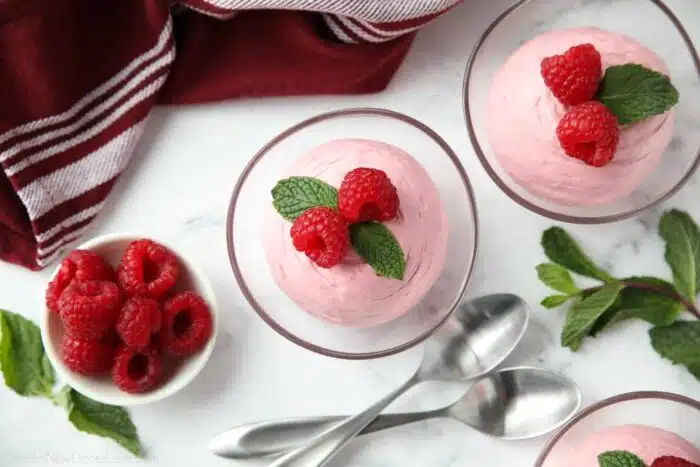 Top view of Raspberry Mousse in a small clear bowls with fresh raspberries and mint on top.