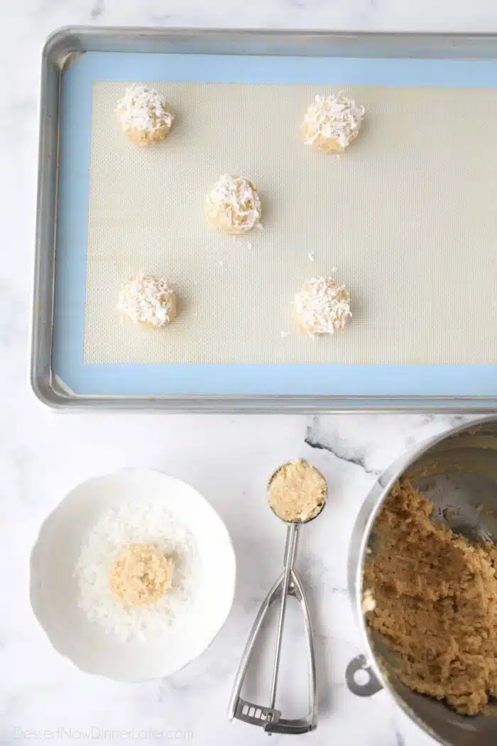 Scooping cookie dough, topping it with coconut, and placing it on a baking tray.