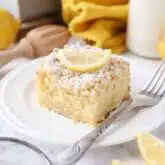 Thick slice of lemon coffee cake on a plate dusted with powdered sugar and a slice of lemon on top.