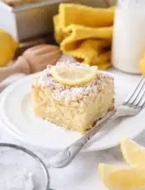 Thick slice of lemon coffee cake on a plate dusted with powdered sugar and a slice of lemon on top.