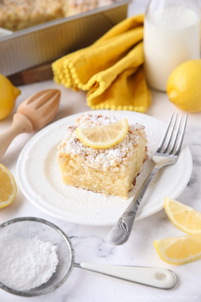 Thick slice of lemon coffee cake on a plate dusted with powdered sugar and a slice of lemon on top.