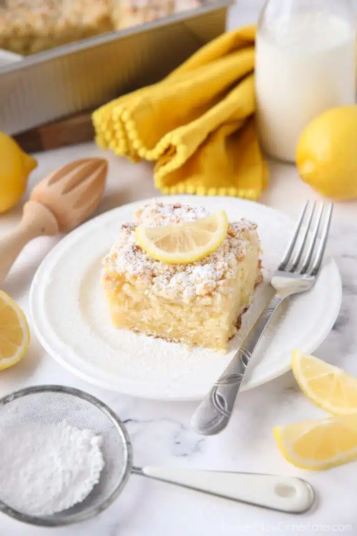 Thick slice of lemon coffee cake on a plate dusted with powdered sugar and a slice of lemon on top.