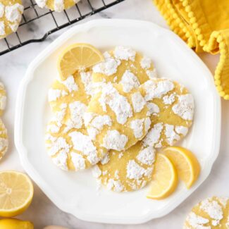 Lemon crinkle cookies on a plate with lemon wedges.