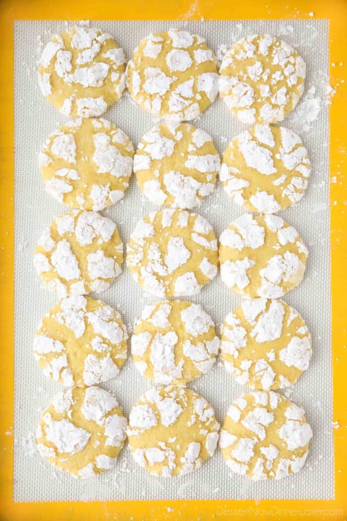 Powdered sugar coated lemon crinkle cookies on a silicone baking mat.