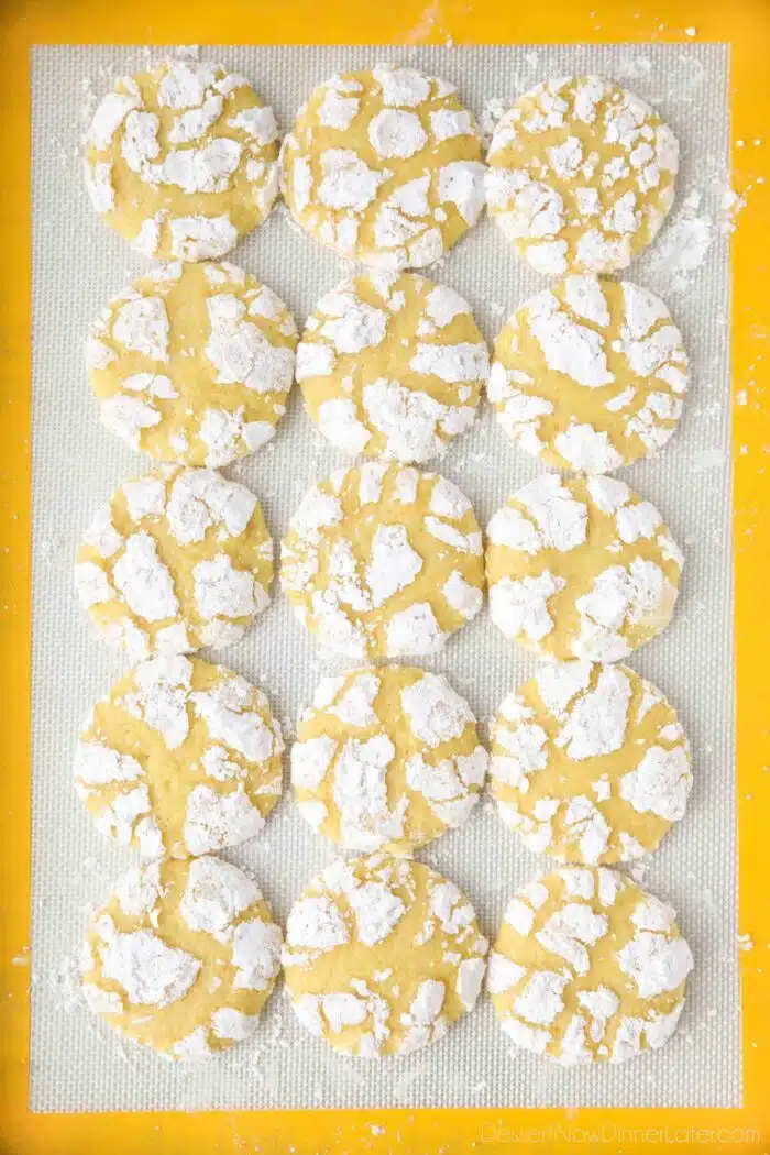 Powdered sugar coated lemon crinkle cookies on a silicone baking mat.