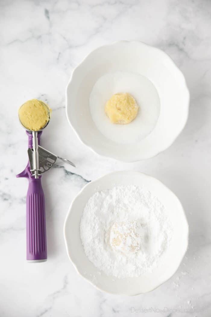 Portioned lemon cookie dough balls being coated in sugar, then powdered sugar.