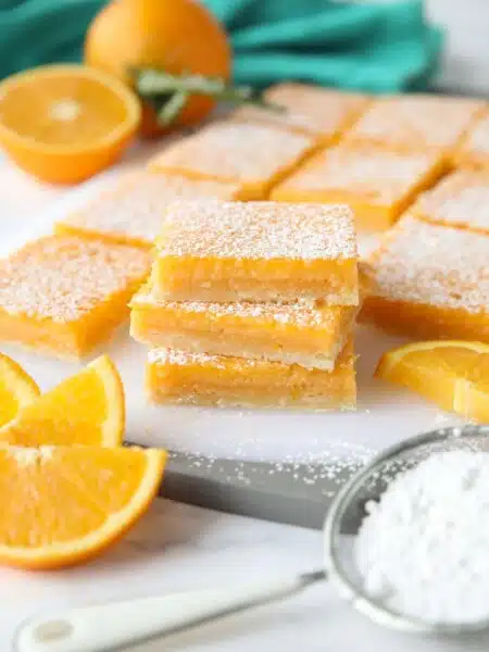 A stack of Orange Bars with powdered sugar dusted on top. (Like lemon bars, but with oranges.)